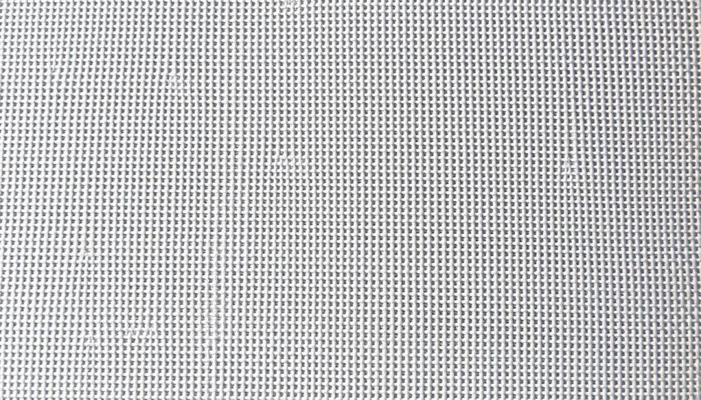 A closeup view of a high-quality canvas material, its tight-woven texture and even weave clearly visible. The surface is smooth, with a slightly rough, matte finish, providing an ideal foundation for intricate needlepoint stitching. Soft, neutral-toned natural fibers, possibly linen or cotton, are illuminated by gentle, even lighting, casting subtle shadows that accentuate the canvas's dimensional qualities. The image is captured at a slightly elevated angle, allowing the viewer to appreciate the canvas's sturdy yet pliable nature, perfectly suited for the precision and detail required in needlepoint embroidery.